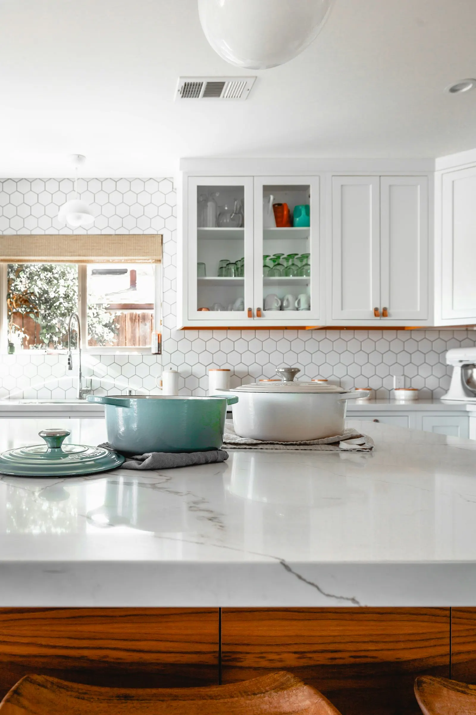 A white kitchen island with marble, wood drawers, and a window over the sink.
