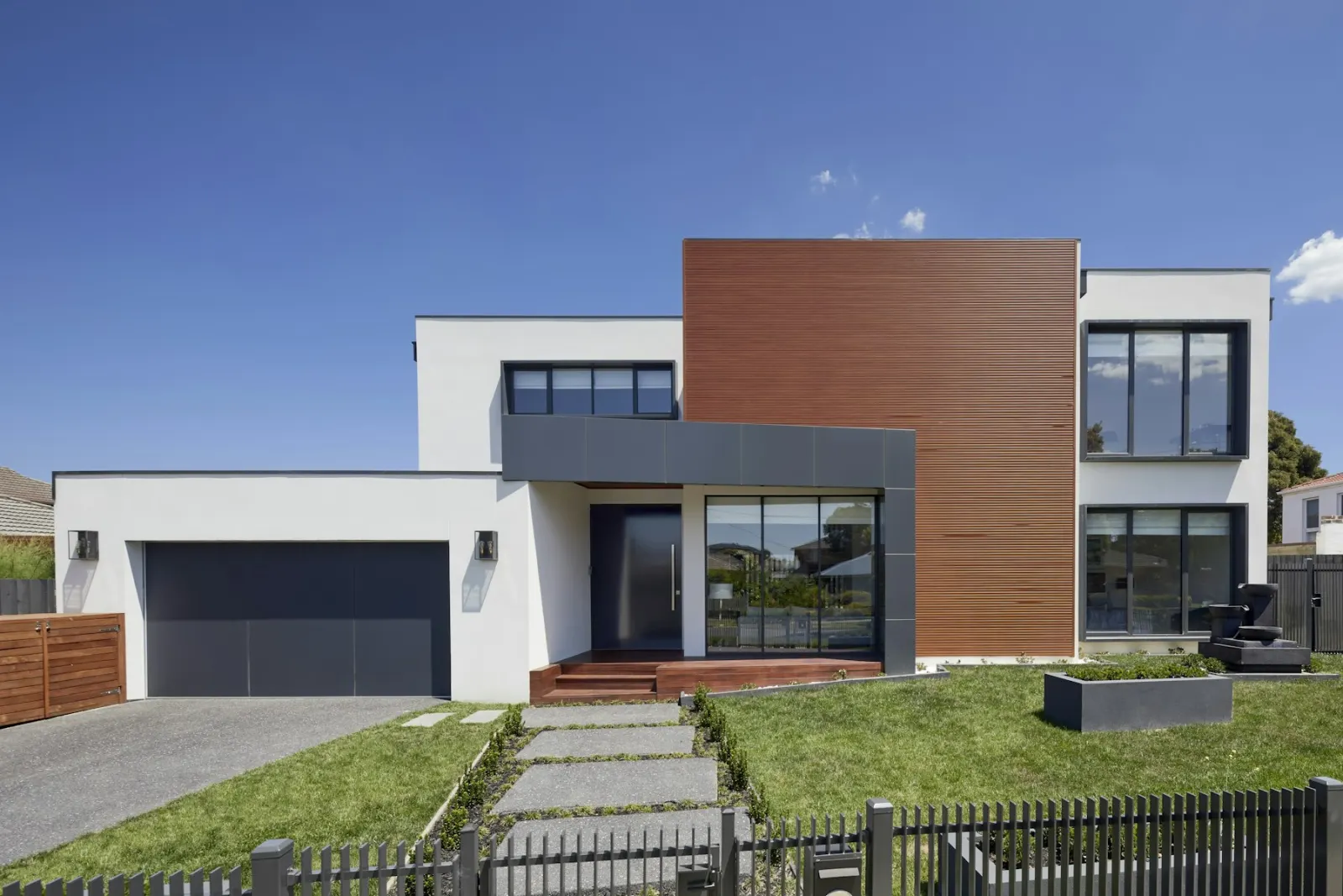 A modern house with white walls, a wood-clad upper bay, and a stone path through the lawn.