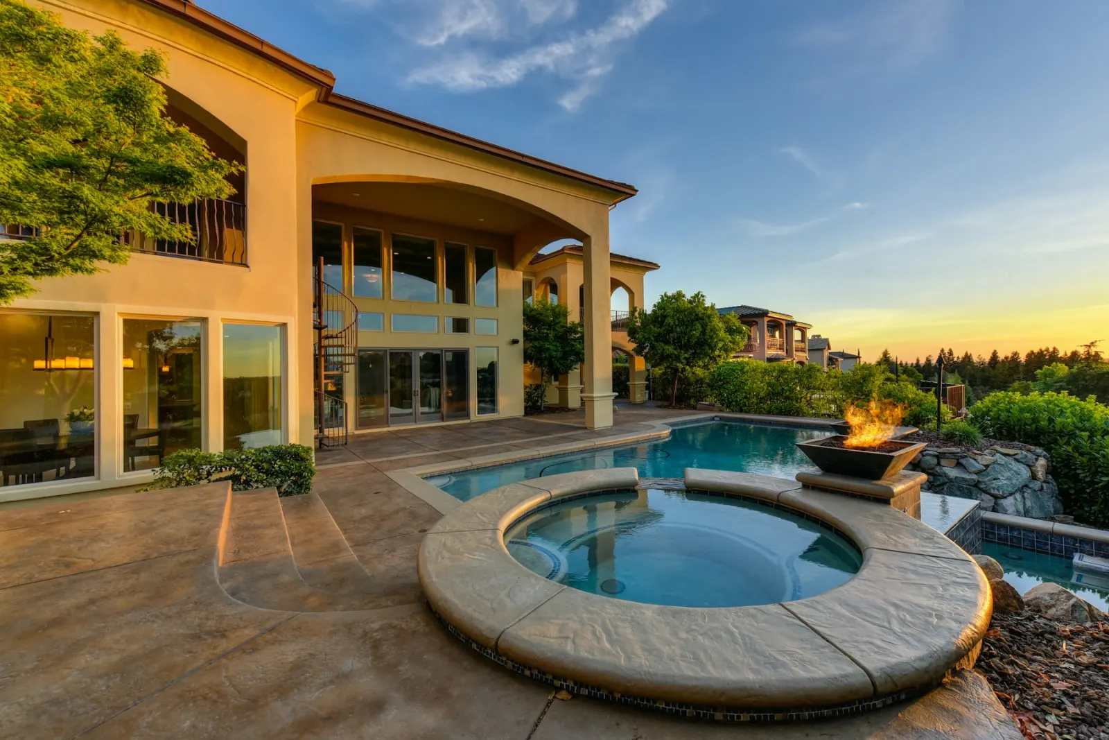 A terrace at sunset with a pool, a spa, and warm light in the windows.